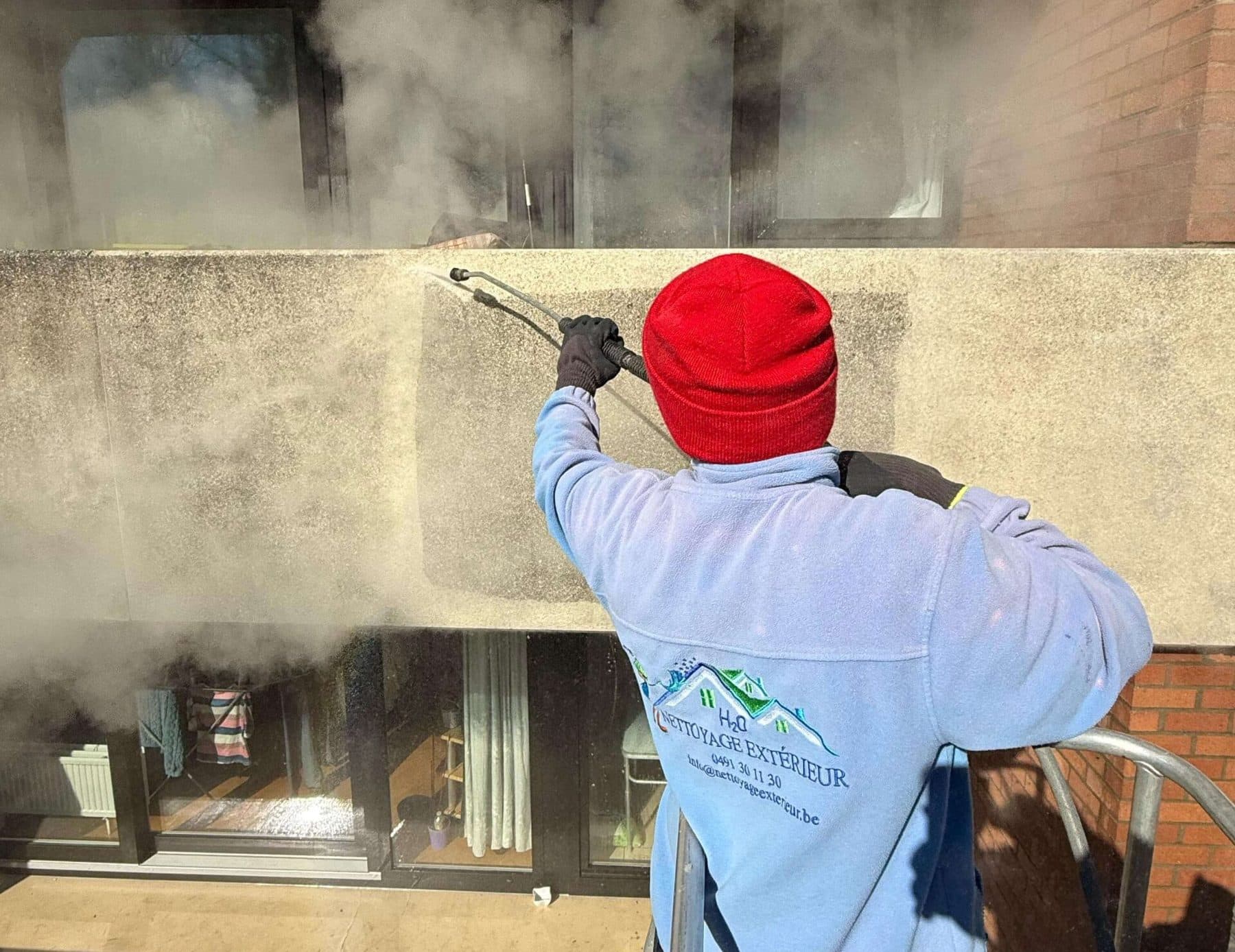 Technicien de Nettoyage Extérieur nettoyant une façade en béton à la vapeur basse pression, la bande déjà traitée est nettement plus claire